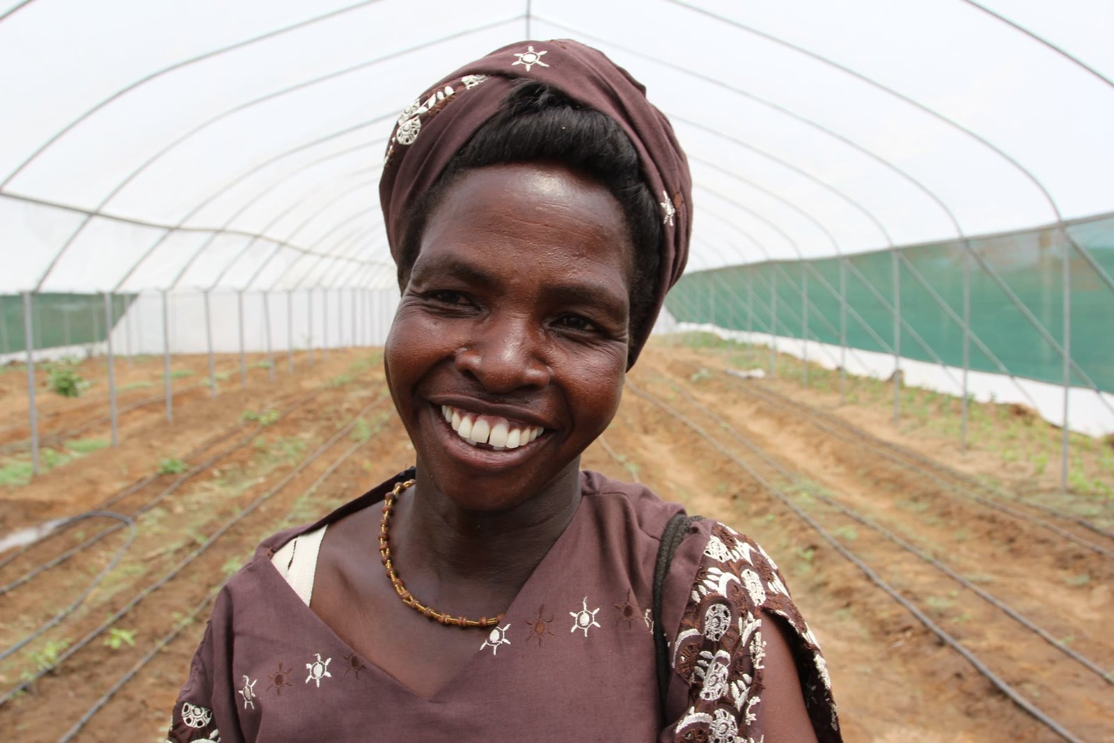 A smiling woman entrepreneur inside a community greenhouse she helped build